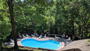 Une piscine entourée d’arbres, avec des chaises longues et une clôture.