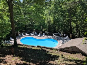 Piscina rodeada por árvores, com espreguiçadeiras e uma vedação.