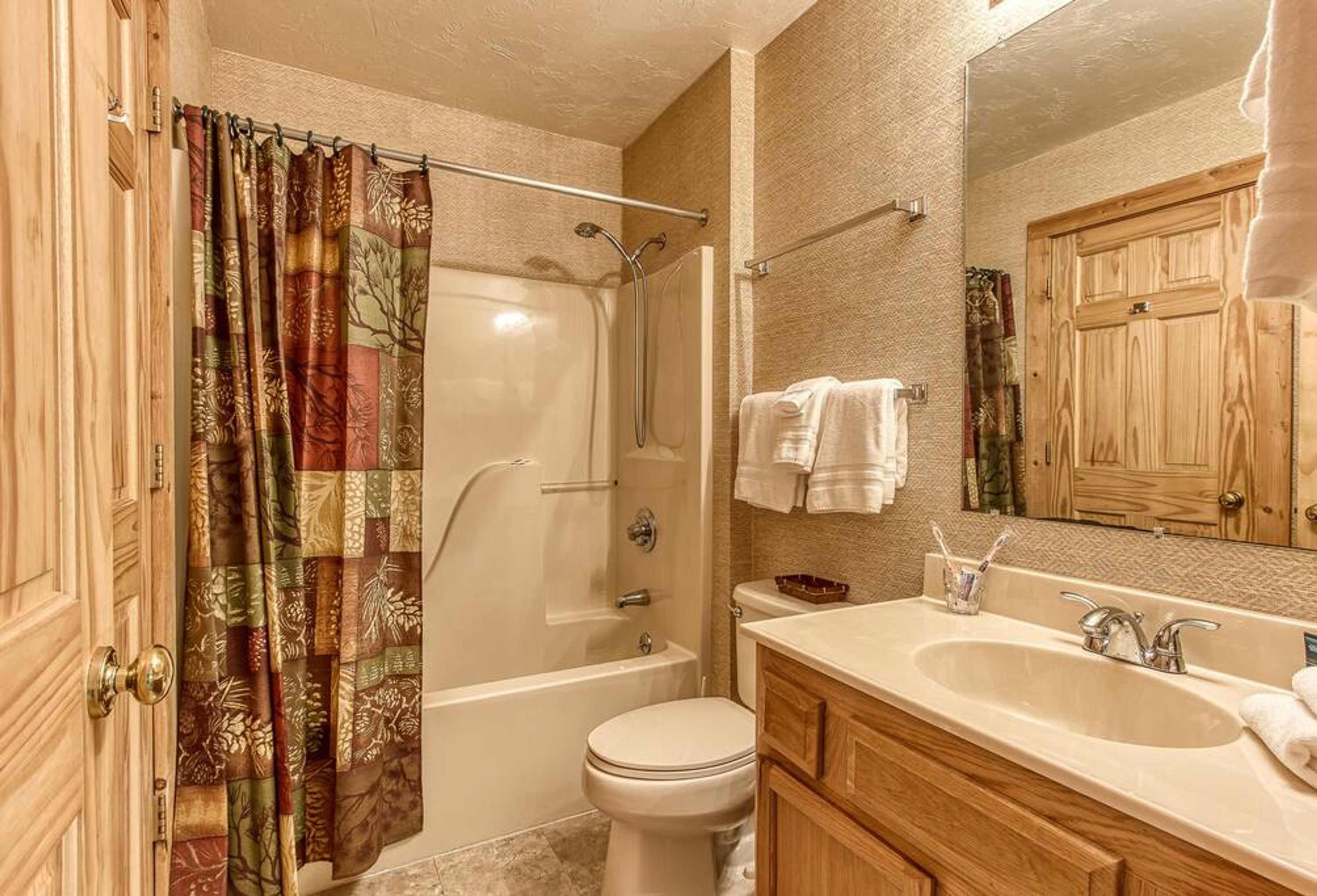 A bathroom with a shower, toilet, sink, and wooden cabinets.