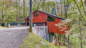 Une cabane rouge avec un porche, entourée d’arbres et bordée d’une allée de gravier.