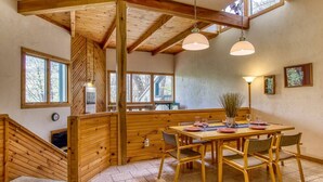 Un intérieur en bois comprenant une table à manger, des chaises, un escalier et une grande fenêtre.