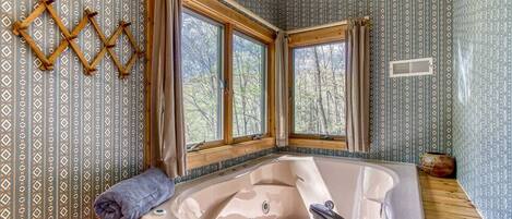 Un baño con una bañera grande, dos ventanas y un papel tapiz estampado.