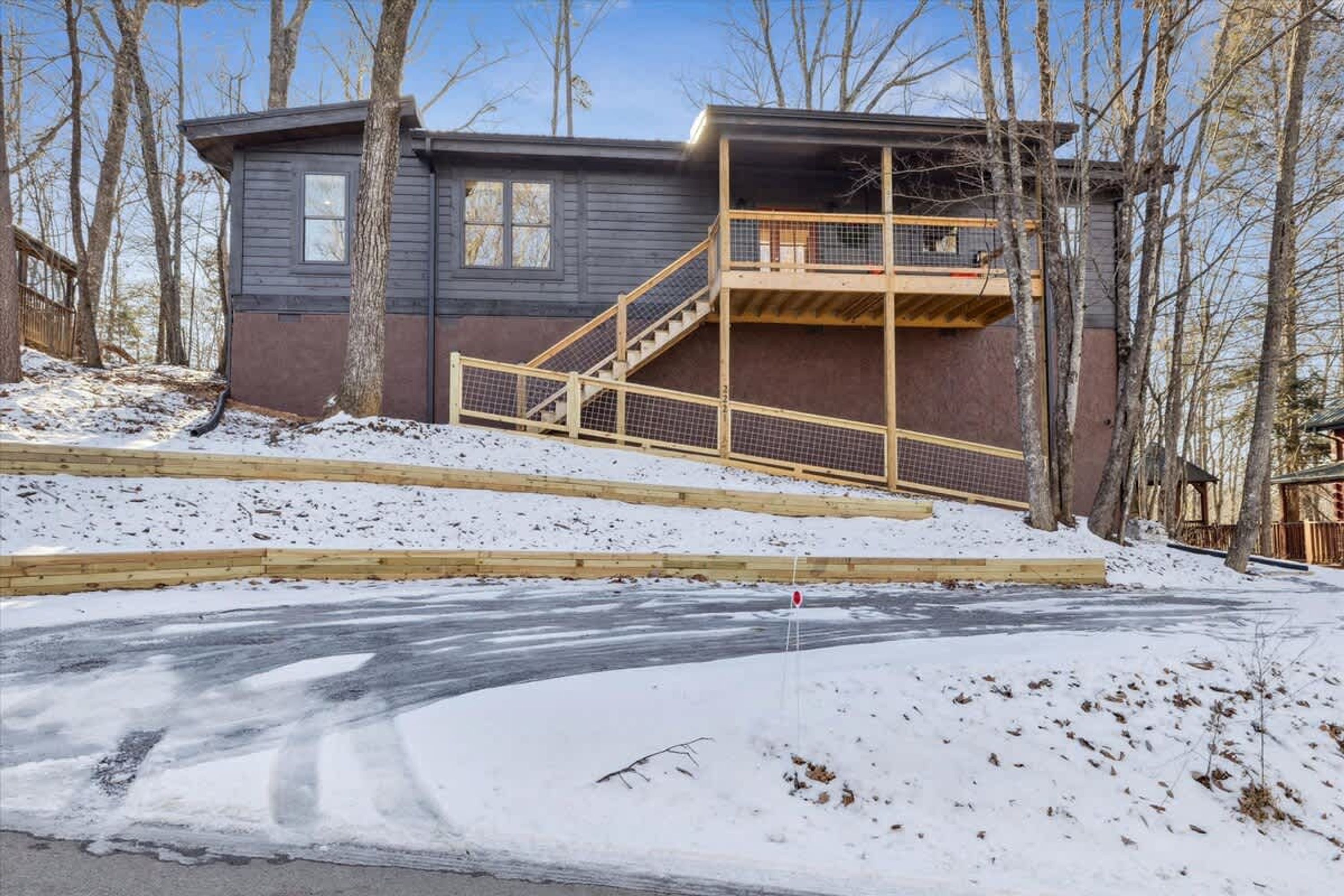 Una cabaña con terraza de madera, una escalera y suelo cubierto de nieve.