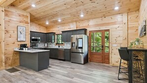 A modern kitchen with wooden walls, a central island, stainless steel appliances, and a bar area. - Bearodise by Beyond Expectations With Hot Tub (Sevierville)