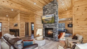 A log cabin interior with a stone fireplace, wooden walls, and a cozy seating area. - Bearodise by Beyond Expectations With Hot Tub (Sevierville)