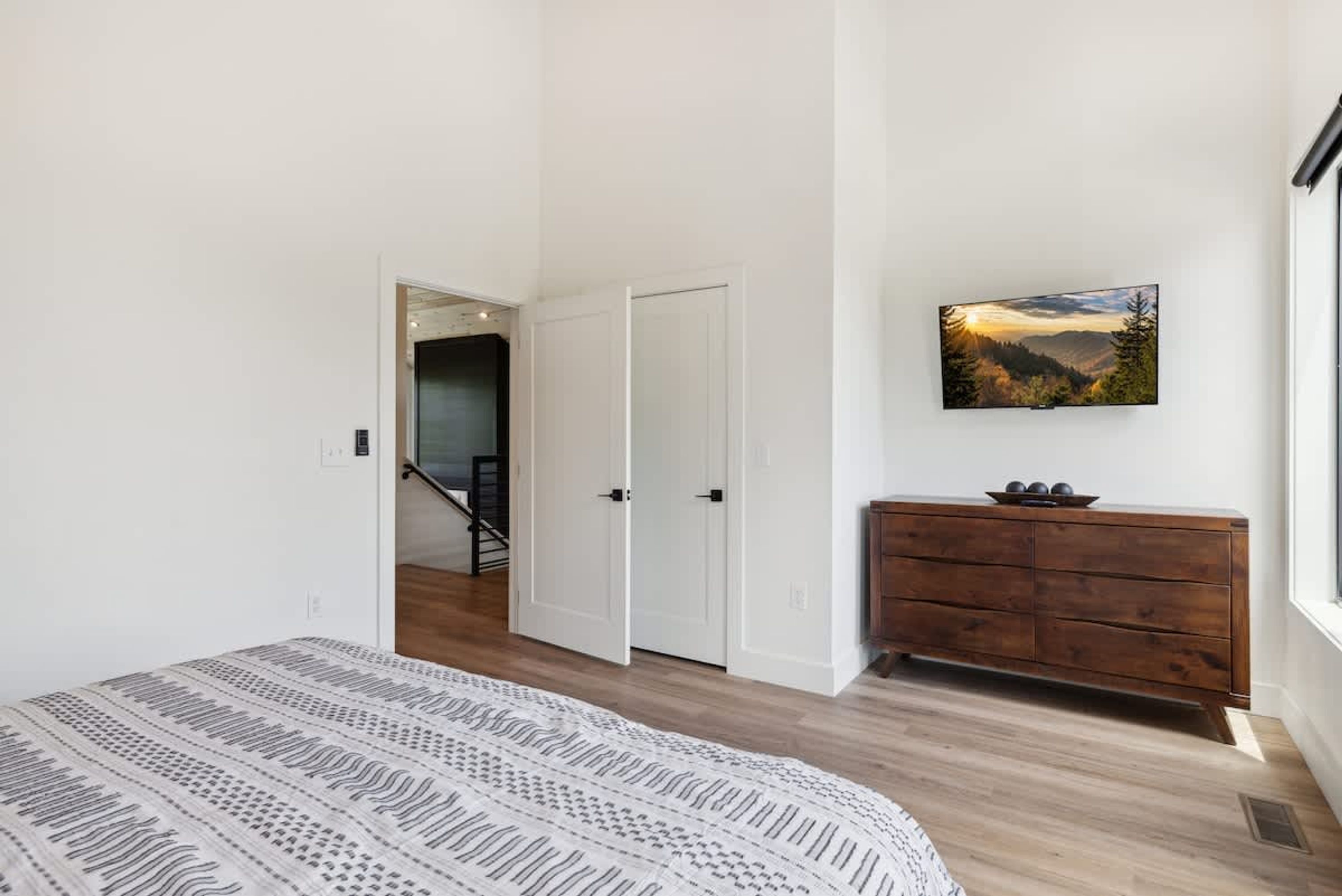 A bedroom with a bed, a dresser, a painting, and a staircase leading to another room.
