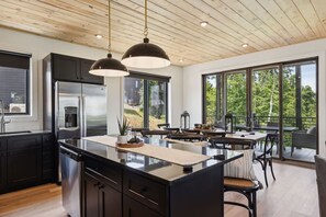 A modern kitchen with a central island, black cabinets, stainless steel appliances, and large windows offering a view of the outdoors. - Mountain Breeze Cabin by Beyond Expectations With Hot Tub (Sevierville)