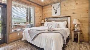 Camera da letto in una baita di legno, con un letto, due lampade da comodino, una finestra con persiane e un'opera d'arte raffigurante una testa di cervo appesa al muro.