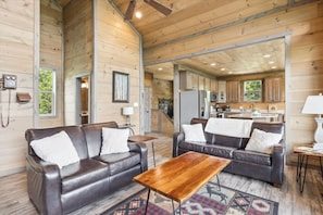 L’intérieur d’une cabine, avec deux canapés en cuir, une table basse en bois et un coin cuisine visible à travers une porte ouverte.