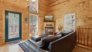 Ein Blockhaus-Interieur mit Kamin, Ledersofa und Blick ins Freie.
