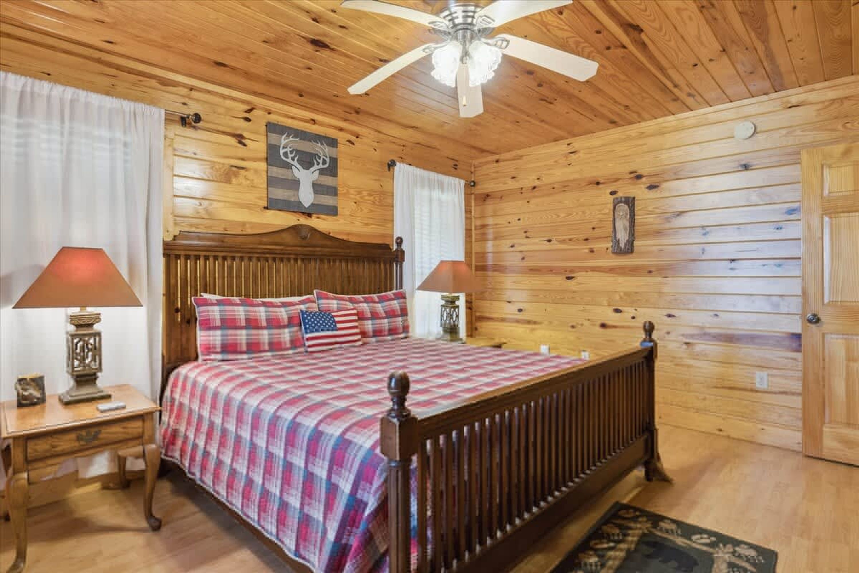 A wooden-paneled bedroom with a bed, two nightstands, a ceiling fan, and a wooden door.