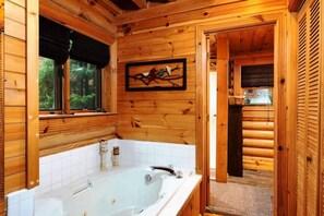 A log cabin bathroom with a large bathtub, wooden walls, and a window. - Rise n Shine Cabin by Beyond Expectations With Hot Tub (Sevierville)