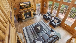 L’intérieur d’un chalet en bois comprend une cheminée, un téléviseur et un coin salon offrant une vue sur l’extérieur.
