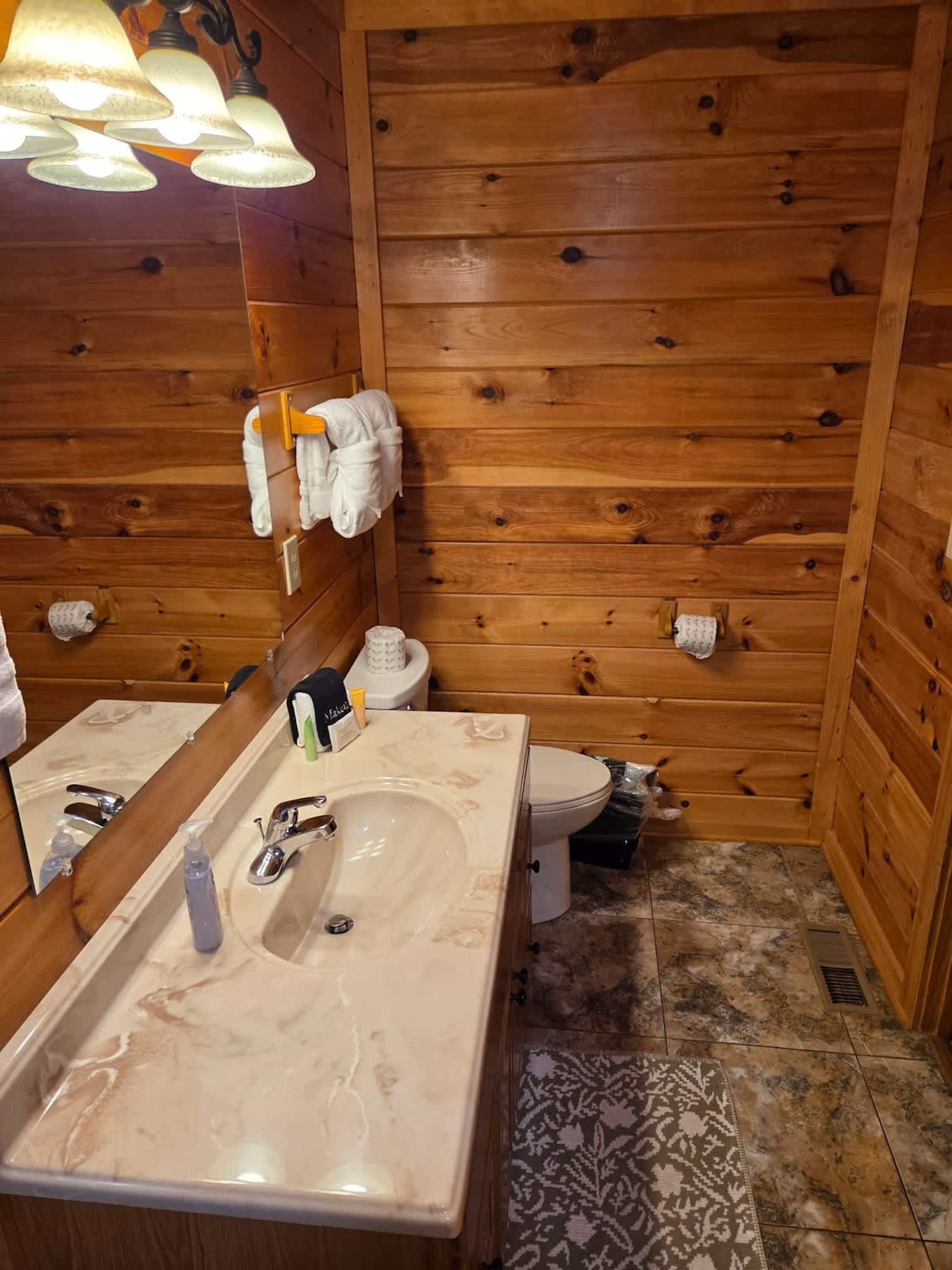A wooden cabin-style bathroom with a marble sink, a toilet, and a towel rack with towels.
