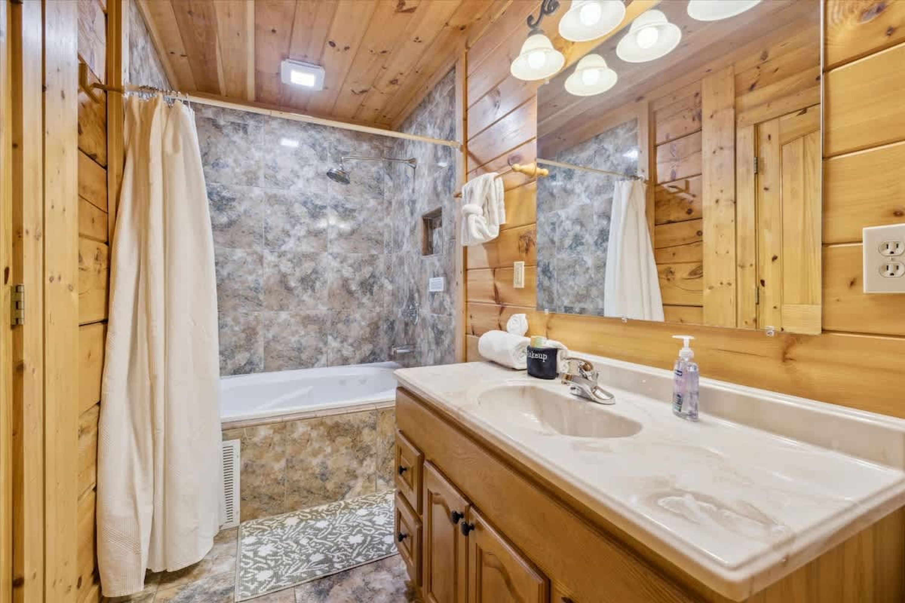 Un baño de cabaña de madera con pared de ducha de mármol, tocador de madera y un espejo grande.