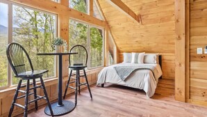 Une cabane en bois avec un lit, deux chaises, une table et de grandes fenêtres.