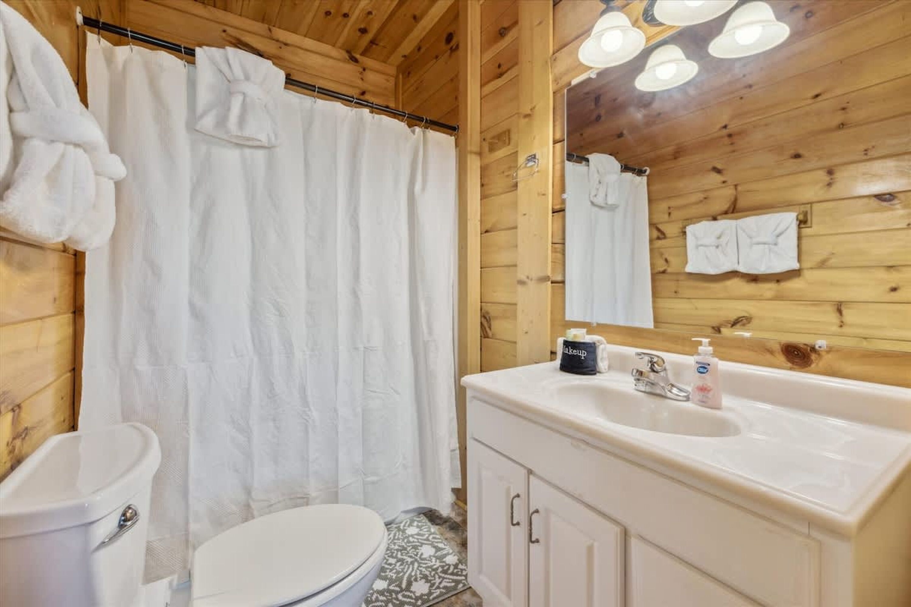 A wooden cabin bathroom with a toilet, shower curtain, sink, and cabinets.