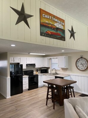 A kitchen with white cabinets, black appliances, a wooden dining table, and a wall clock.