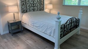 Une chambre à coucher avec un lit blanc, deux tables de chevet et une fenêtre avec des stores.