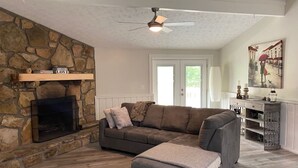 Un salon avec une cheminée en pierre, un canapé gris et un ventilateur de plafond.
