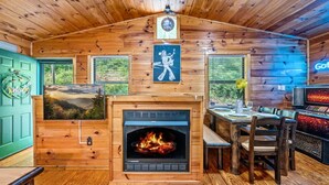 A cabin interior with a fireplace, wooden walls, a dining area, and a view of the outdoors. - A Little Bit of Country by Beyond Expectations (Pigeon Forge)
