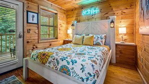 A wooden cabin bedroom with a bed, two nightstands, a neon sign, and a window with blinds. - A Little Bit of Country by Beyond Expectations (Pigeon Forge)