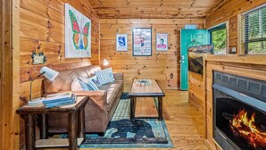 A cozy cabin interior with a wooden interior, a sofa, a coffee table, a fireplace, and a door. - A Little Bit of Country by Beyond Expectations (Pigeon Forge)