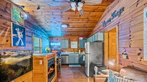 A cabin interior with a fireplace, kitchen, and a cozy seating area. - A Little Bit of Country by Beyond Expectations (Pigeon Forge)