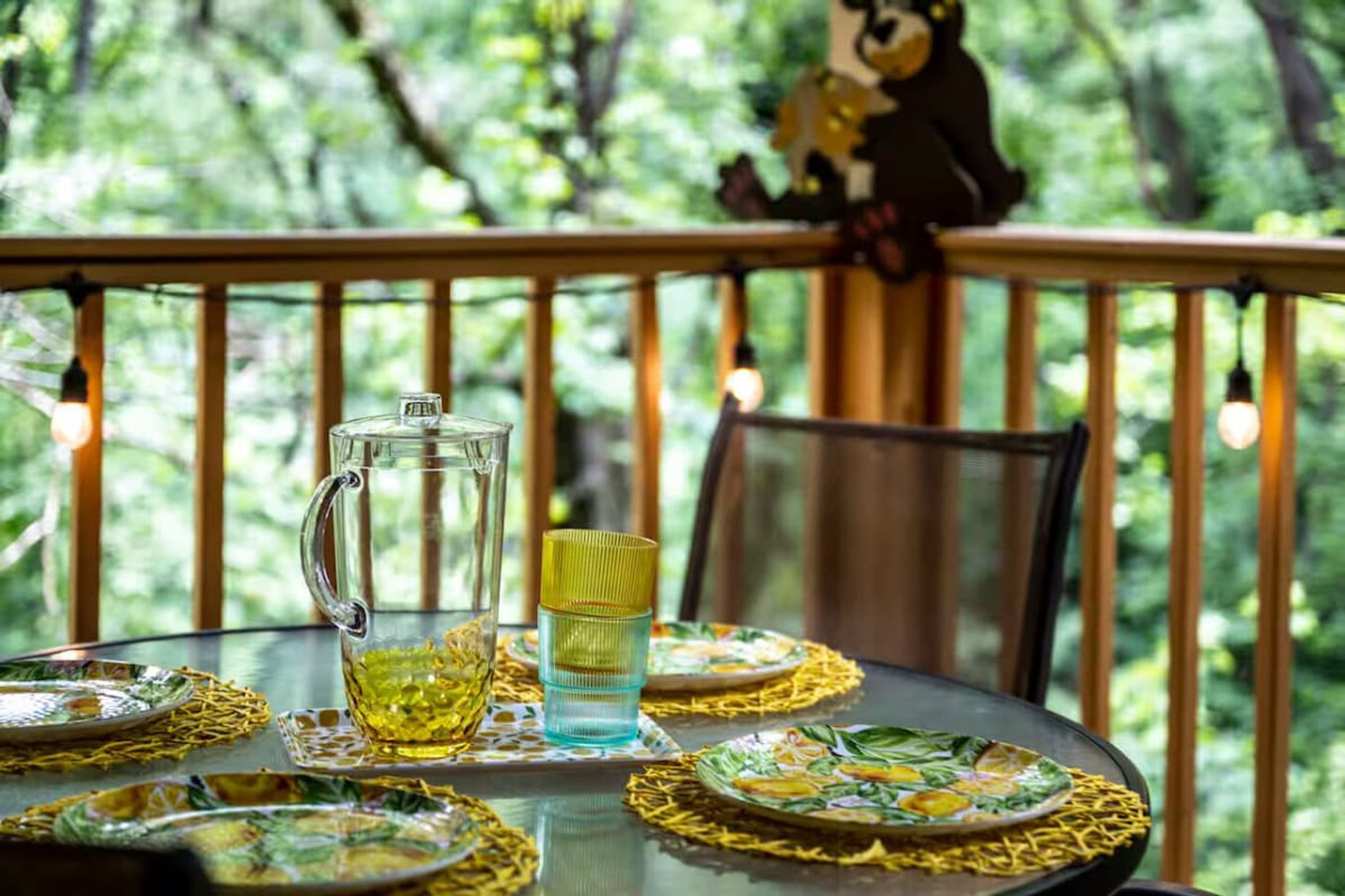 A table set outdoors with a glass pitcher, a glass, and plates on a table with a yellow table runner.