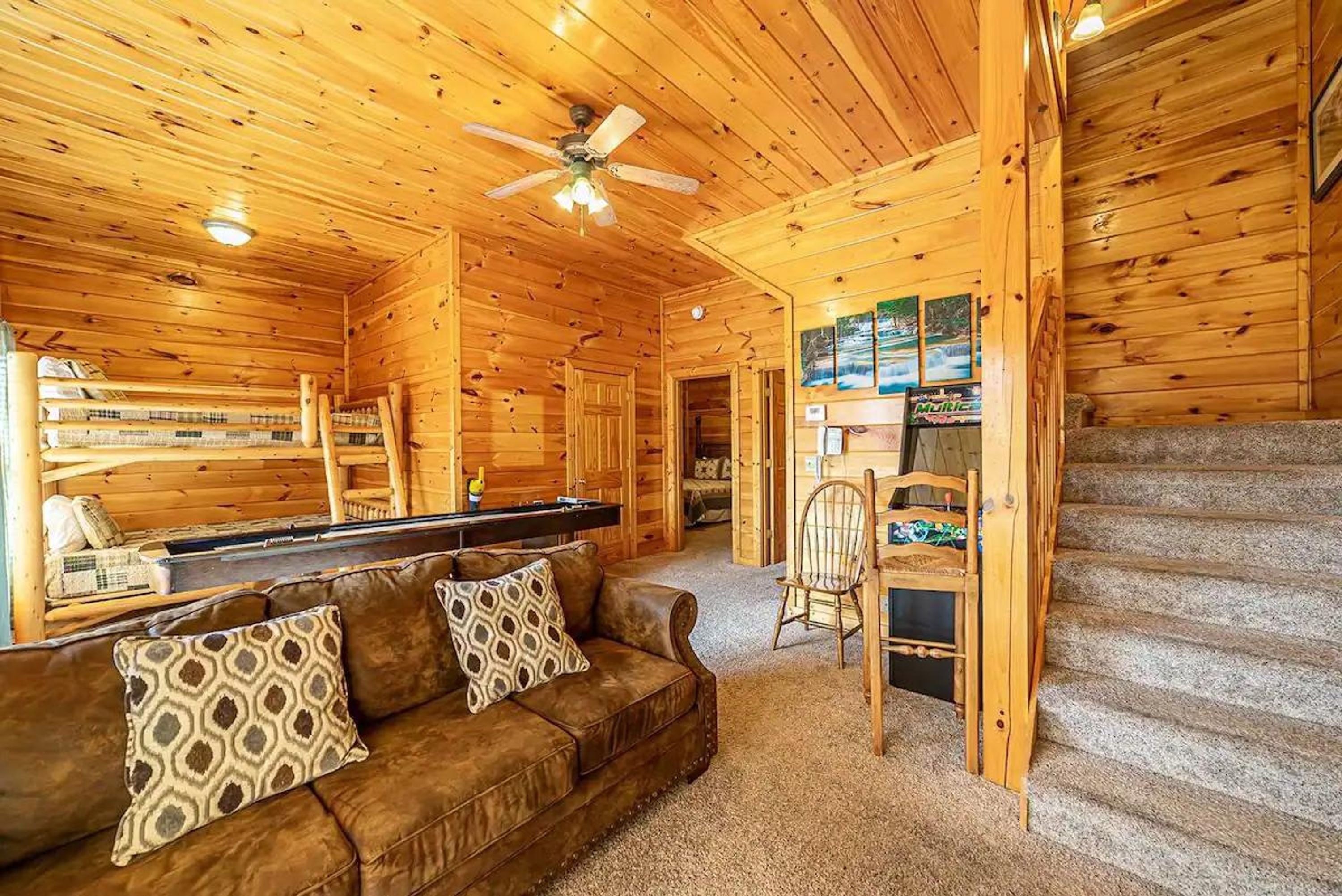 A wooden cabin interior with a sofa, a dining table, and a ceiling fan.