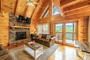 A wooden cabin interior with a stone fireplace, a sofa, a coffee table, and a TV mounted on the wall. - Joes Place Cabin by Beyond Expectations With Hot Tub (Pigeon Forge)