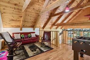 A wooden interior with a red sofa, a rocking chair, and a foosball table. - Hideaway at the River by Beyond Expectations (Sevierville)