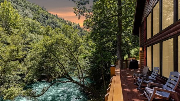 A wooden deck with lounge chairs overlooking a river and forested area. - Hideaway at the River by Beyond Expectations (Sevierville)