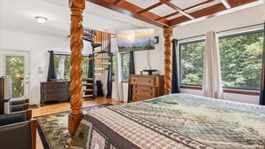 A bedroom with a four-poster bed, a wooden staircase, a large window with curtains, and a view of trees. - Hideaway at the River by Beyond Expectations (Sevierville)