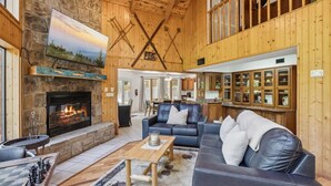 A cozy interior with a stone fireplace, wooden ceiling beams, a dining area, and a kitchen with wooden cabinets. - Hideaway at the River by Beyond Expectations (Sevierville)