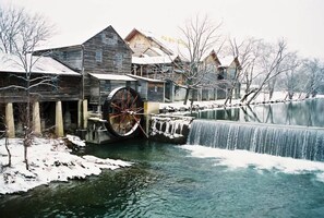 A rustic wooden building with a large water wheel, a river, and snow-covered trees. - Hawks Nest Cabin by Beyond Expectations With Hot Tub (Sevierville)