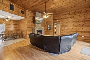 A log cabin interior with a fireplace, leather sofa, wooden dining table, and chairs. - Hawks Nest Cabin by Beyond Expectations With Hot Tub (Sevierville)