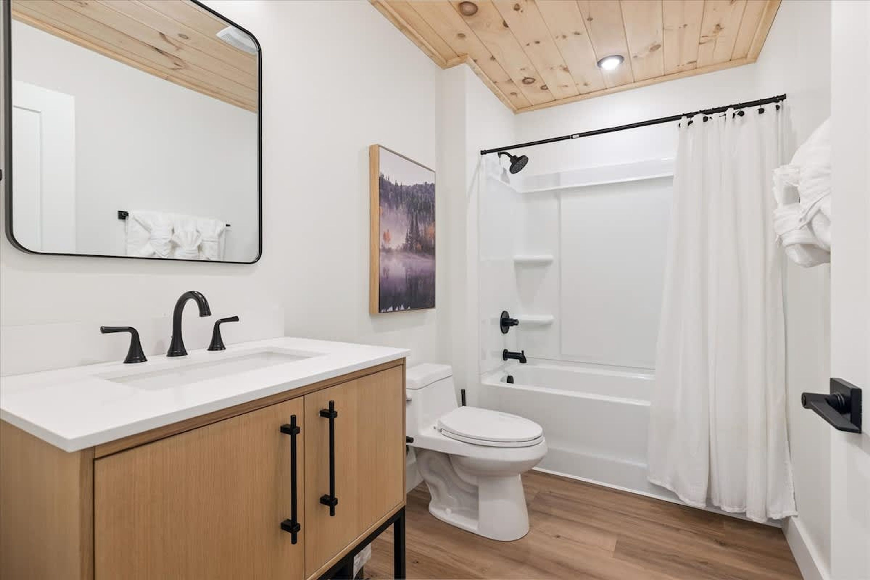 Et badeværelse med et trækommode, en hvid vask, toilet, badekar og bruseforhæng.