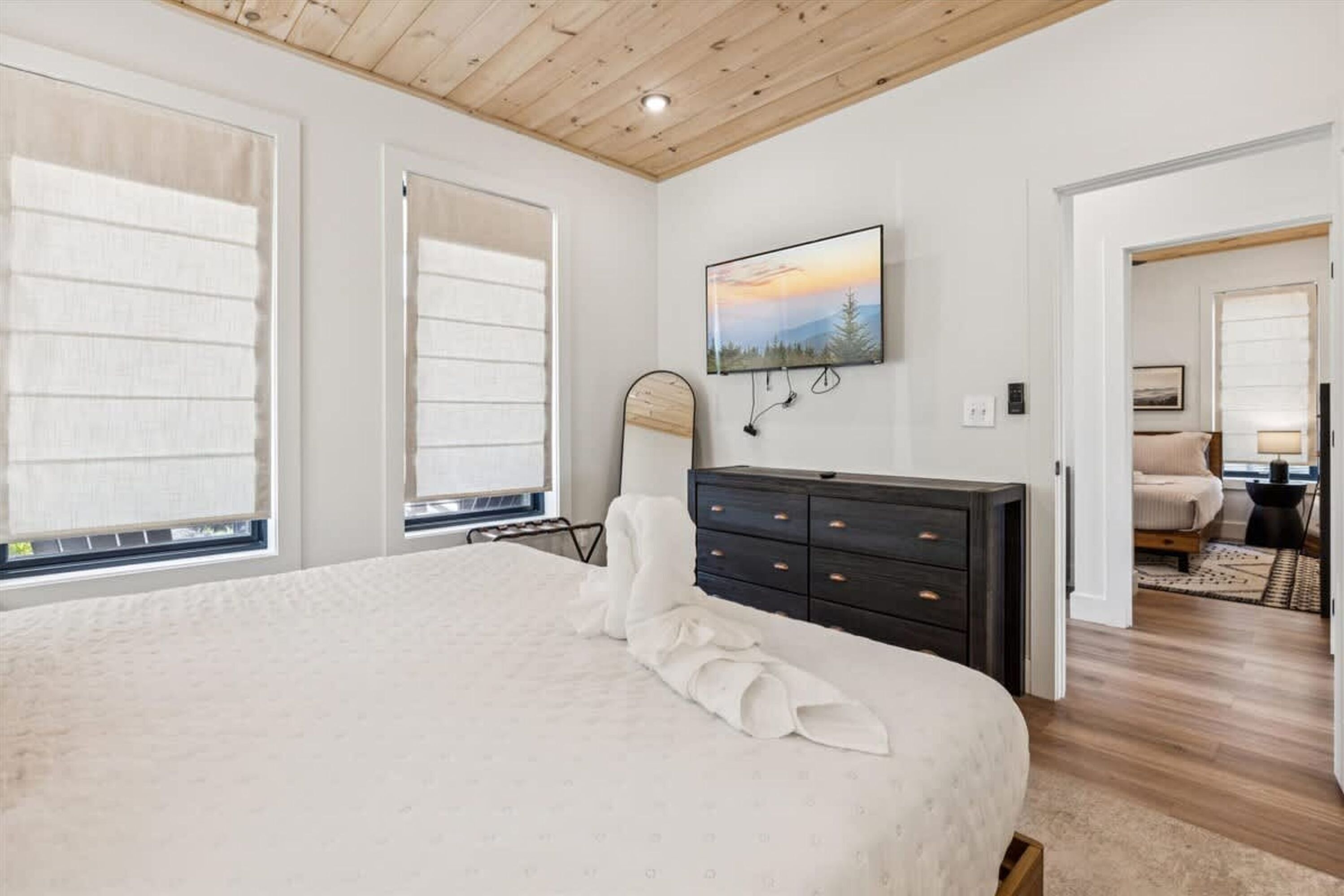 A bedroom with a large bed, a dark dresser, a TV mounted on the wall, and a window with blinds.