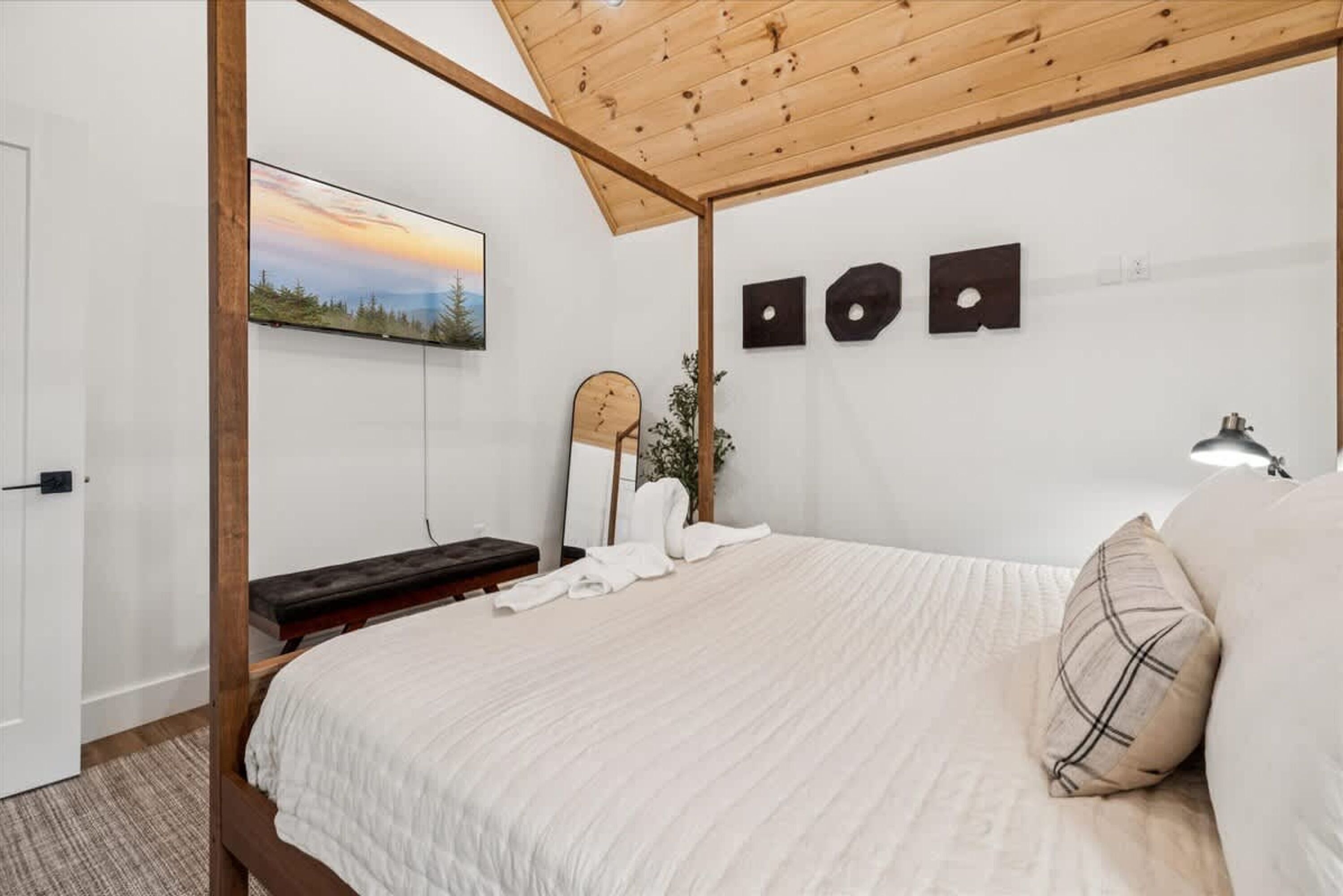 A bedroom with a bed, a bench, a mirror, and a painting on the wall.