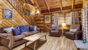A log cabin interior with a wooden staircase, leather sofas, a wooden coffee table, and plaid curtains. - Laceys Place by Beyond Expectations With Hot Tub (Sevierville)