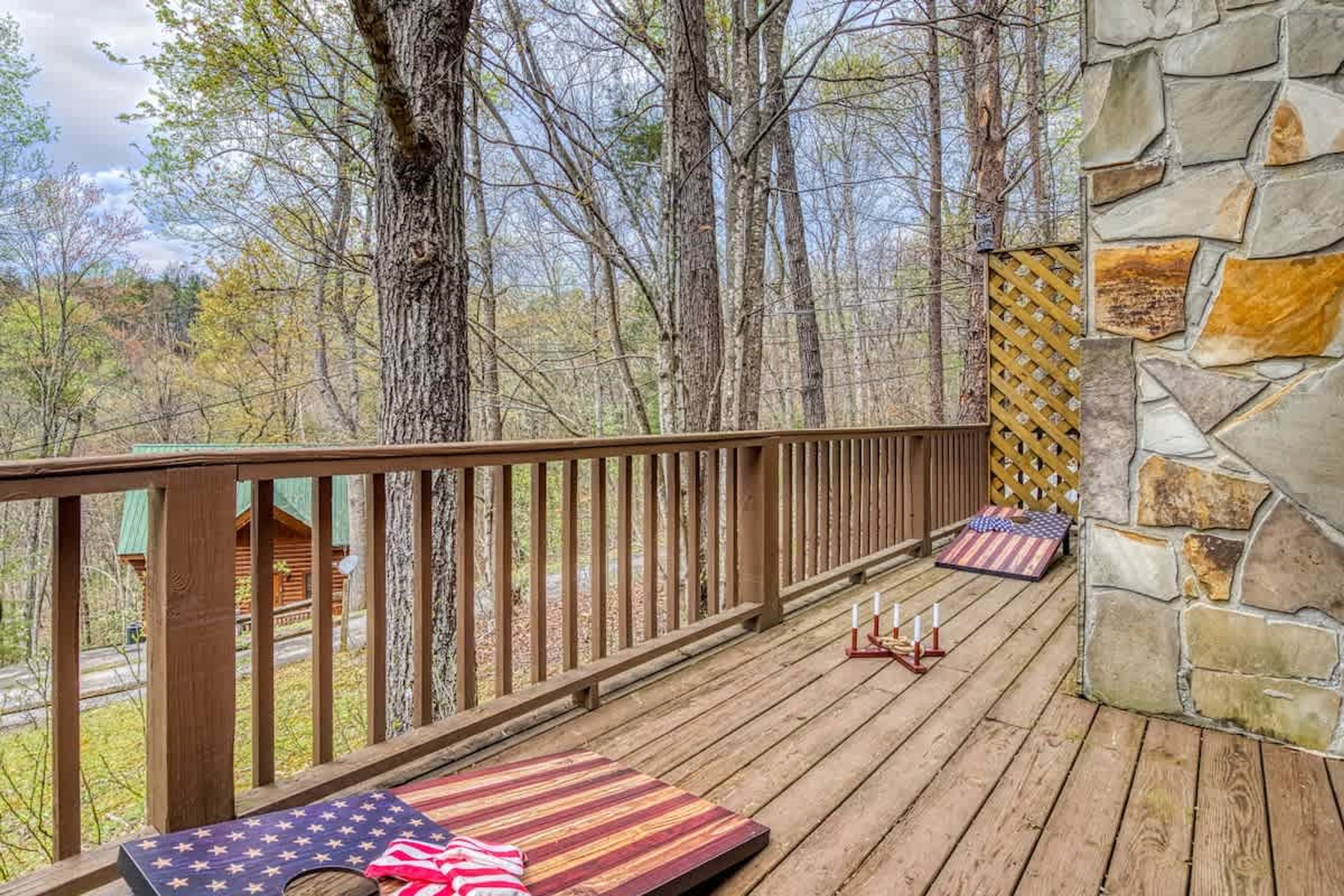 A wooden deck with a stone wall, a bench with an American flag, and a view of trees and a cabin.