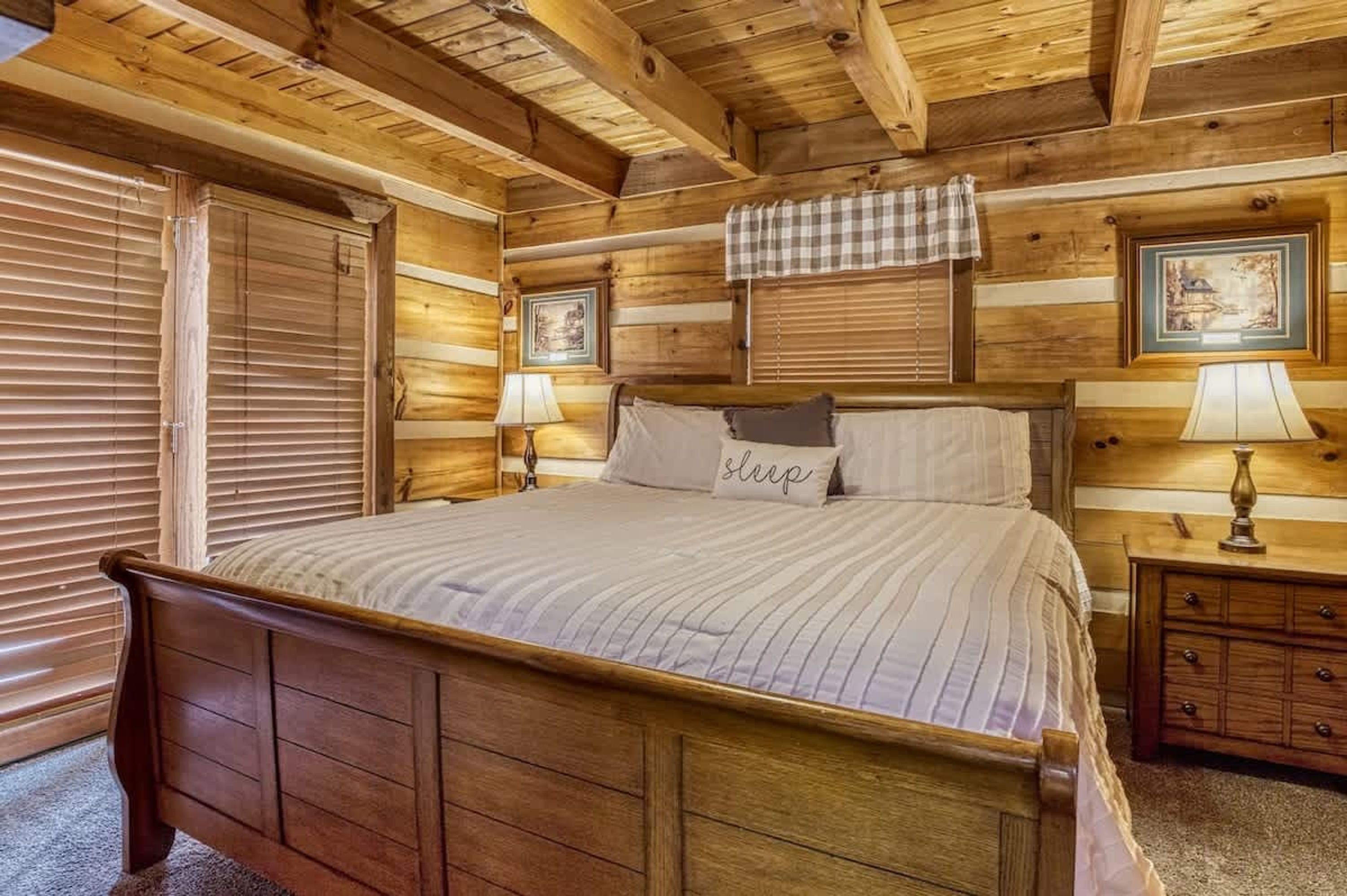A wooden-paneled bedroom with a bed, two bedside tables, and a window with blinds.