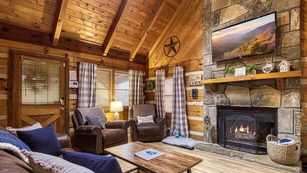 A cozy cabin interior with a fireplace, leather furniture, and a television mounted on the wall. - Laceys Place by Beyond Expectations With Hot Tub (Sevierville)