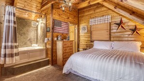 A log cabin bedroom with a wooden ceiling, a ceiling fan, a bed, a vanity with a mirror, a shower, and an American flag. - Laceys Place by Beyond Expectations With Hot Tub (Sevierville)