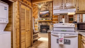 A cabin interior with a stone fireplace, wooden walls, a television, and a kitchen with a stove and microwave. - Laceys Place by Beyond Expectations With Hot Tub (Sevierville)