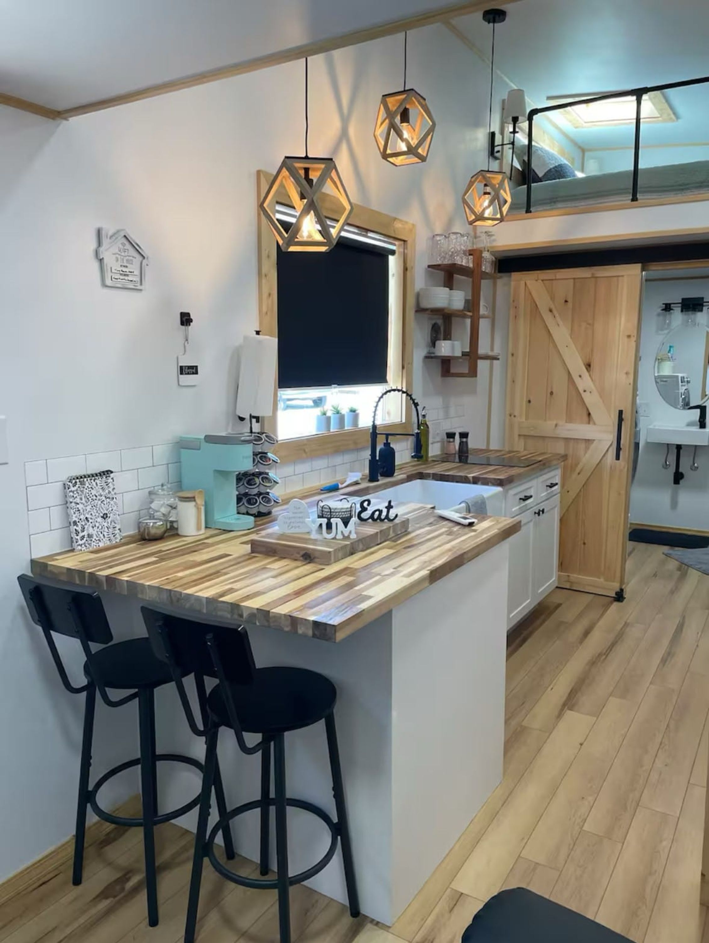 A modern kitchen with a wooden island, black bar stools, pendant lights, and a skylight.