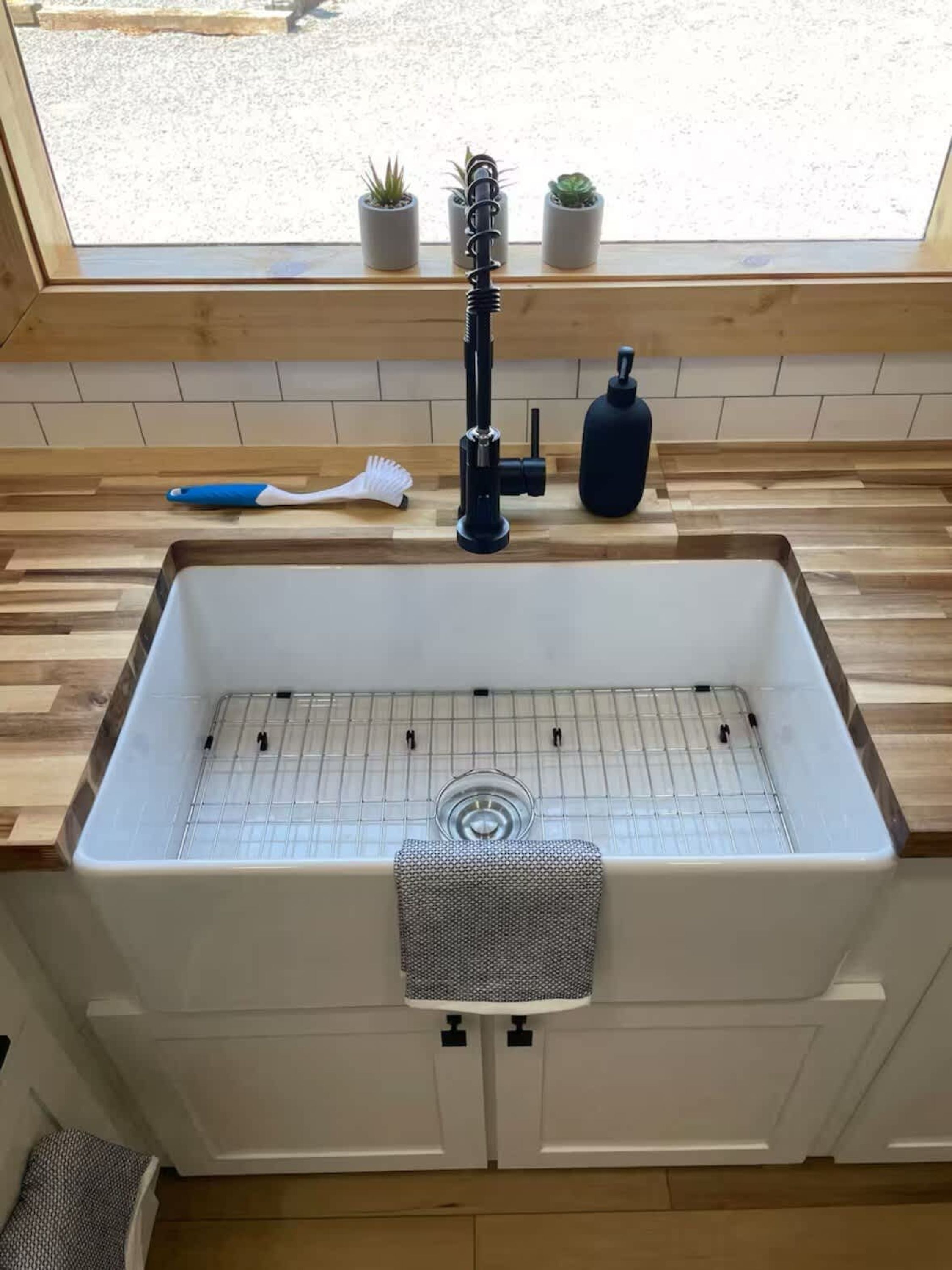 Een keuken met een wit spoelbak, een houten aanrechtblad en een raam boven de spoelbak.