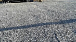 Ein schwarzer Wohnmobil mit zwei Fenstern und einer Tür, geparkt auf Kies. Im Hintergrund Bäume und Berge.