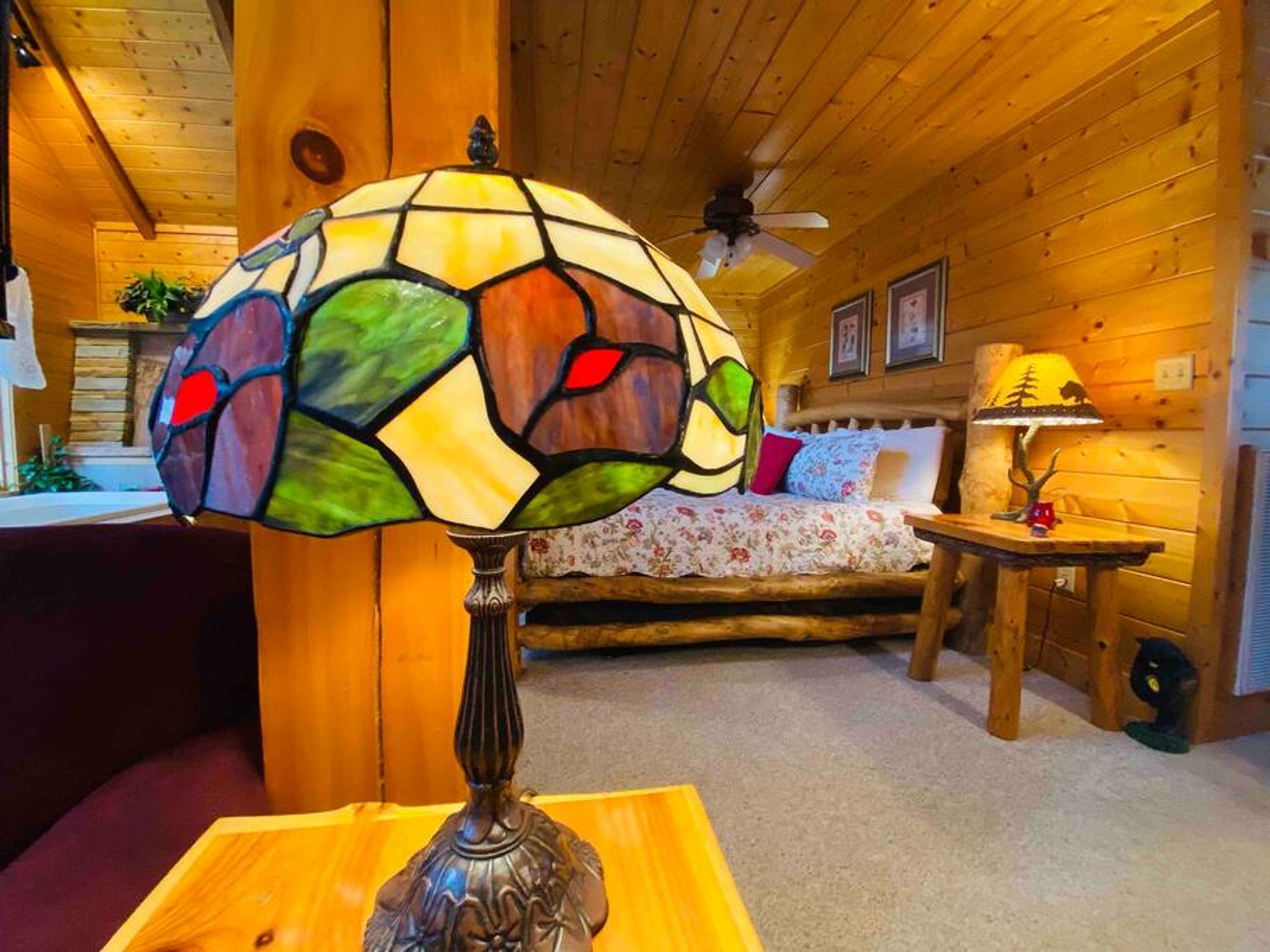 A cozy room with a bed, a wooden ceiling fan, and a stained glass lamp.